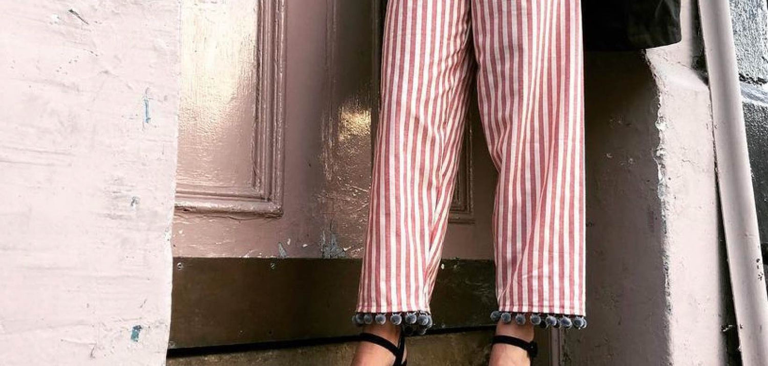 Woman wearing a pair of pink and white striped Party Pants, with grey pom pom trim
